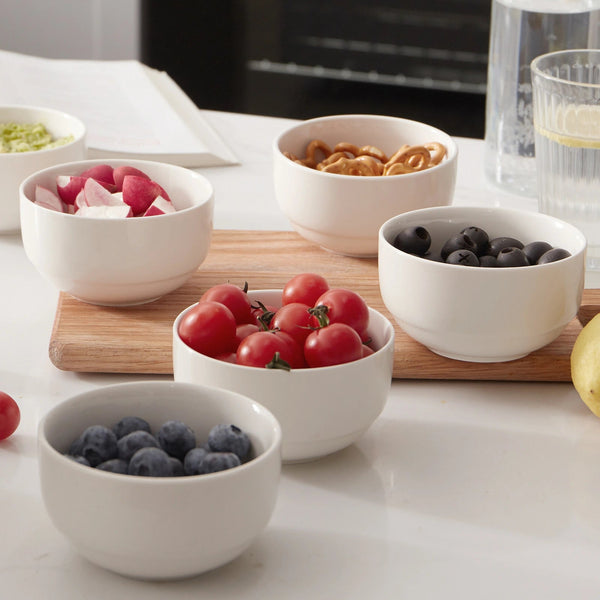 Set of white bowls containing fruits and snacks on a kitchen counter.