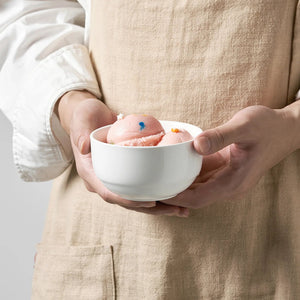 Person holding a white bowl with pink bath bombs against a neutral background