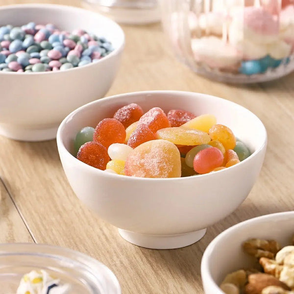 White bowl filled with colorful gummy candies on a wooden table.