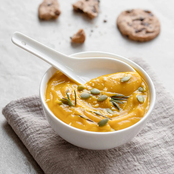 Bowl of pumpkin soup with a spoon on a textured surface