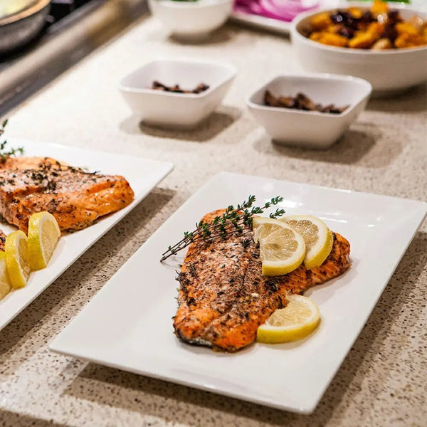 Plated salmon with lemon slices on a countertop with additional plates and bowls in the background.