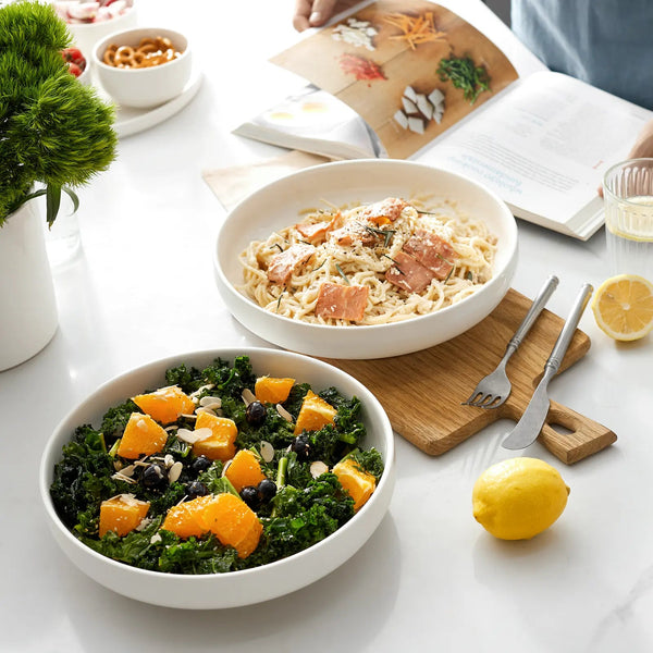 Two bowls of salad on a table with a book and lemon