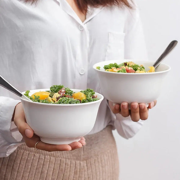 Person holding two bowls of salad with a plain background