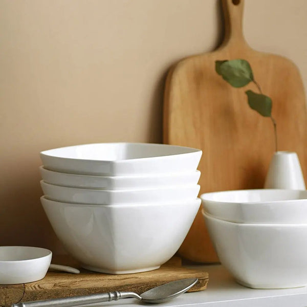 Stack of white bowls on a wooden surface with a cutting board in the background.