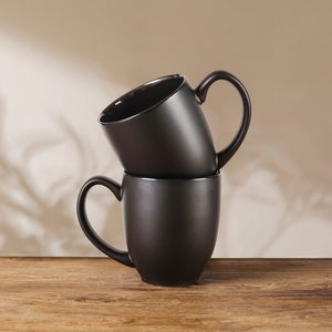 matte black coffee mugs stacked on a wooden surface with a beige wall background