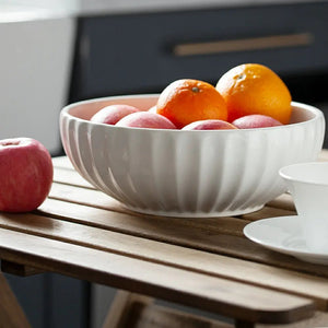 White ceramic bowl with apples and oranges on a wooden table