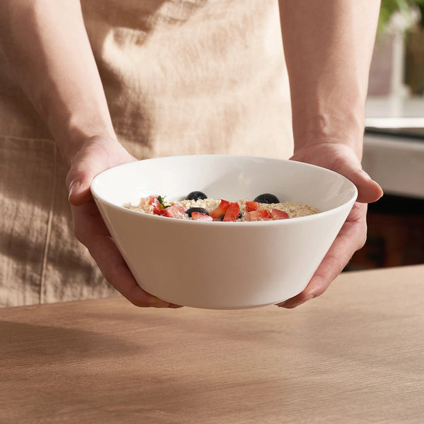 Person holding a white bowl with oatmeal and berries on a wooden surface