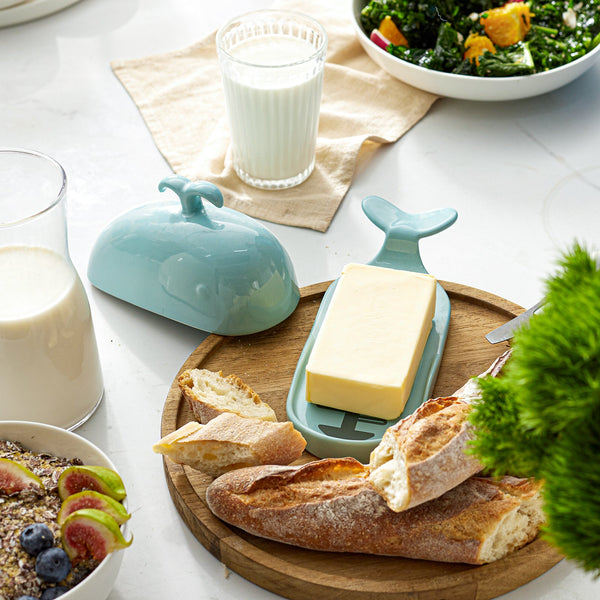 Butter dish with whale design on a wooden board with bread and milk, on a white table.