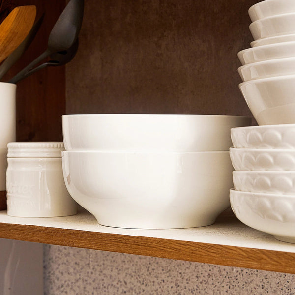 White ceramic bowls and containers on a wooden shelf against a brown wall.