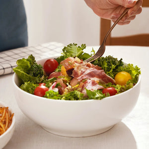 Bowl of salad with greens, tomatoes, and prosciutto being eaten with a fork.