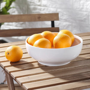 White bowl filled with oranges on a wooden table outdoors