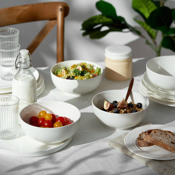 Table setting with bowls of food, glasses, and a bottle on a light surface.