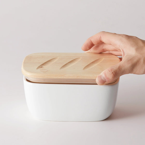 White container with a wooden lid being held by a hand on a light gray background