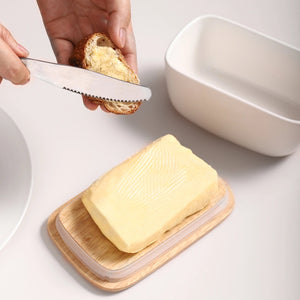 Butter on a wooden board with a knife and bread in the background