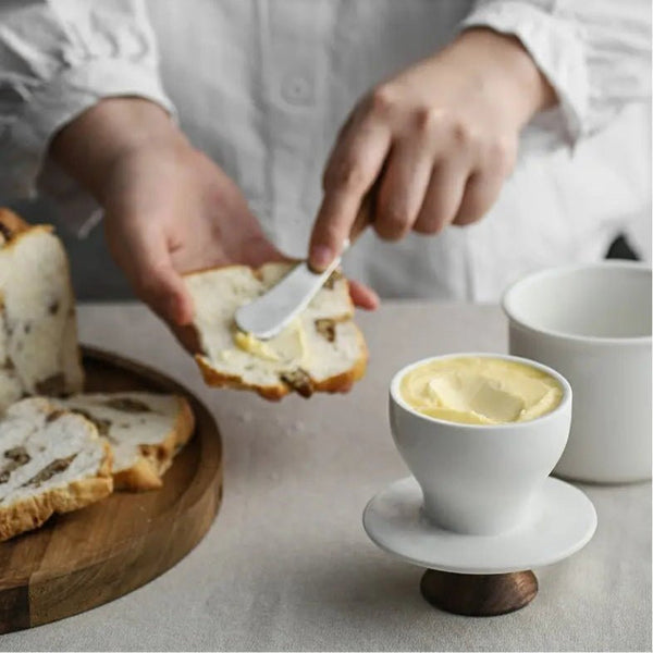 Person spreading butter on a slice of bread with a small bowl of butter nearby.