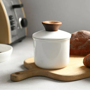 White ceramic container with wooden lid on a wooden cutting board in a kitchen setting