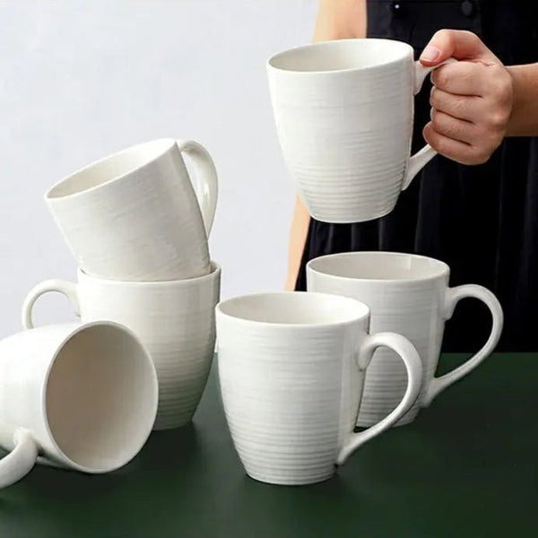 White ceramic mugs on a green surface with a person holding one mug.