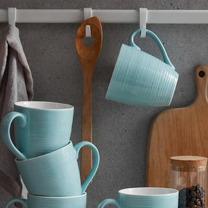 Stack of turquoise coffee mugs with a wooden spoon and cutting board on a gray wall.