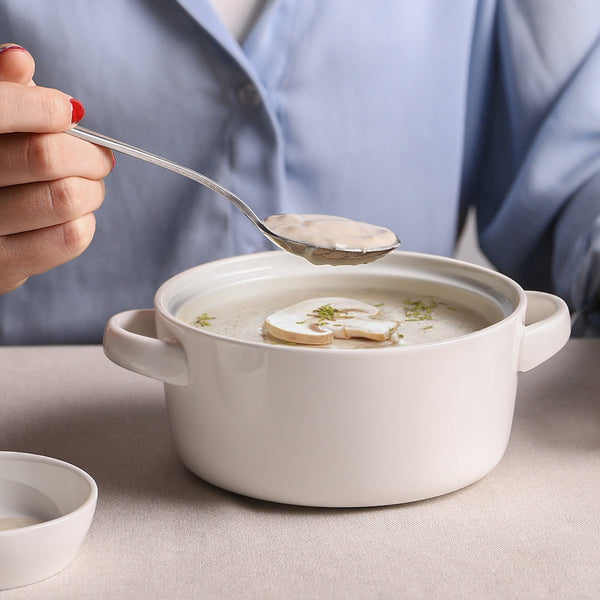 Person holding a spoon over a bowl of soup with a neutral background
