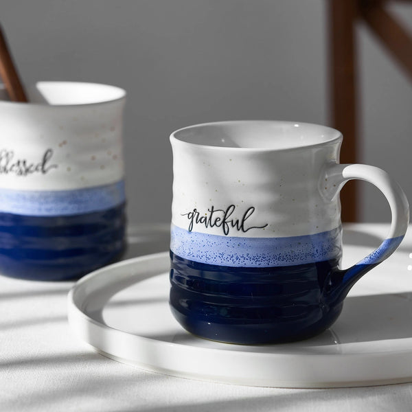 Two blue ceramic coffee mugs with spoons inside, placed on a white plate.