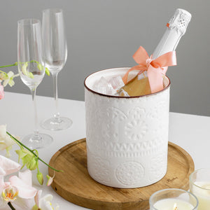 Bottle of champagne in a decorative ice bucket with a pink bow, surrounded by glasses and flowers on a table.