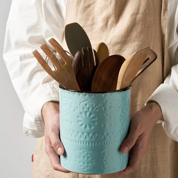 Person holding a turquoise container with wooden utensils against a neutral background