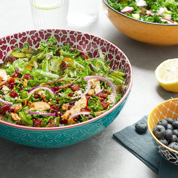 Salad in a decorative bowl on a table with a lemon and blueberries.