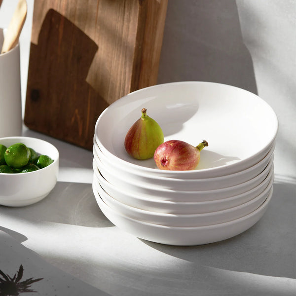 Stack of white ceramic pasta bowls with figs on a gray surface