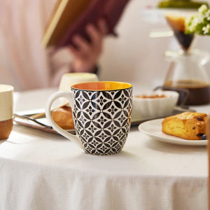 Colorful patterned coffee mug on a table with pastries and a book in the background