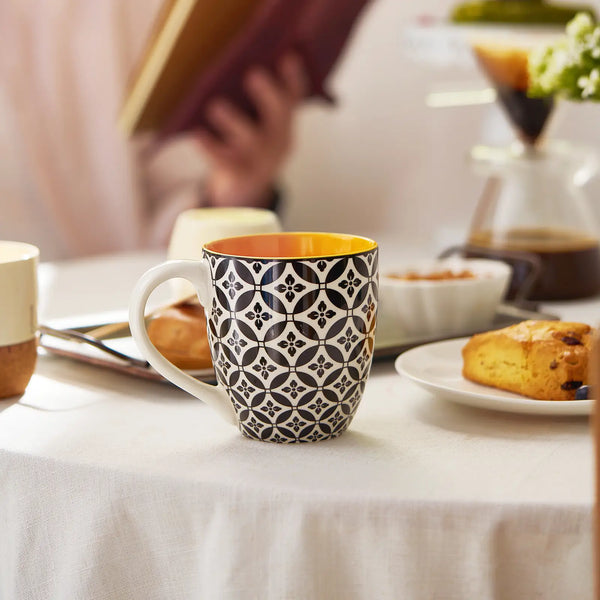 Colorful patterned coffee mug on a table with pastries and a book in the background