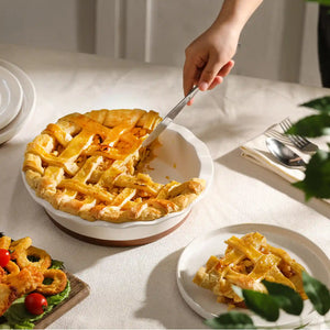 Person cutting into a pie on a table with round baking dish.
