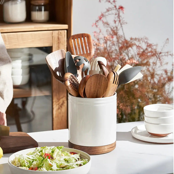 Set of wooden kitchen utensils in a white container on a table with a blurred background