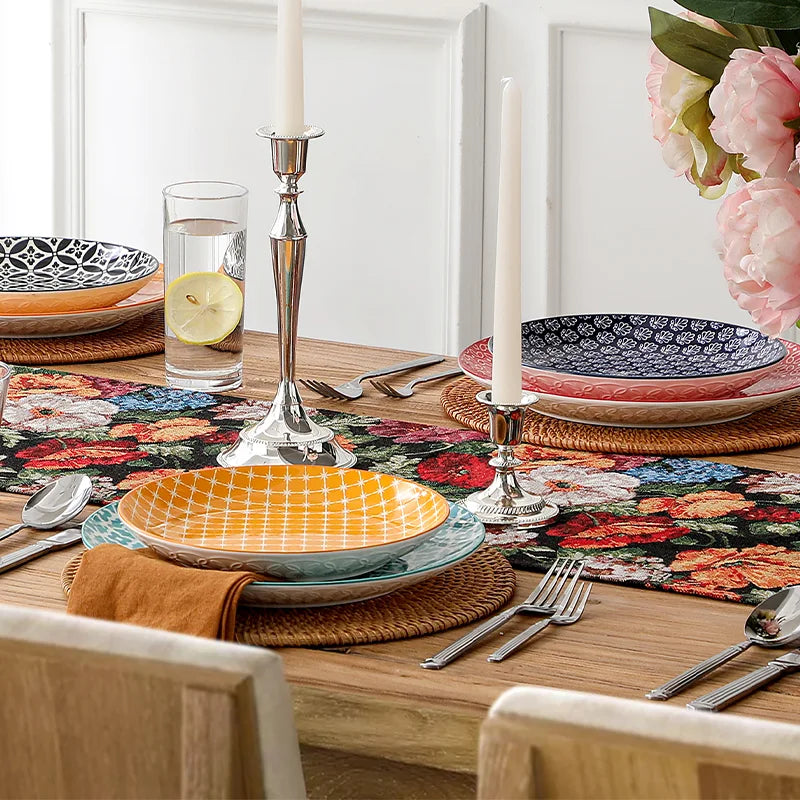 Dining table setting with colorful plates, floral placemats, and candlesticks.