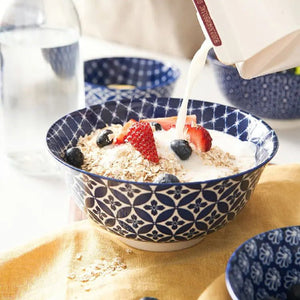 Blue patterned bowl with a cereal and fruit dish, milk being poured in.