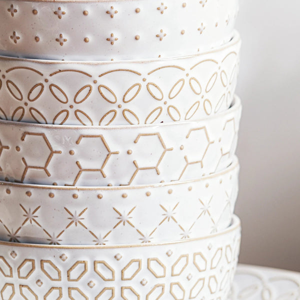 Stack of white ceramic pots with geometric patterns on a neutral background