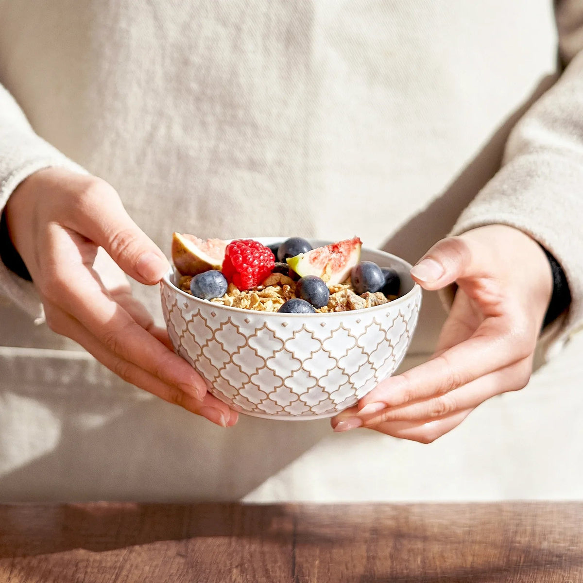 Person holding a bowl of cereal with fruits on a wooden table