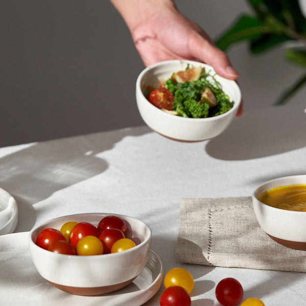 Person holding a bowl of salad with cherry tomatoes on a table with other bowls and a napkin.