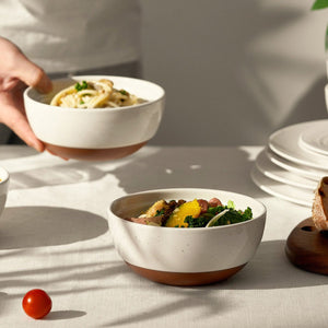 Person holding a bowl of pasta with another bowl of salad on a table.