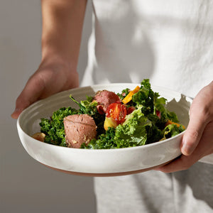Person holding a bowl of salad with greens and meat.