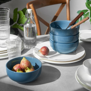 Blue ceramic bowls on a table with glasses, a bottle, and fruit.