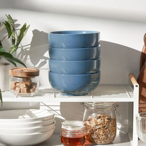 Stack of blue bowls on a kitchen shelf with jars and a plant.