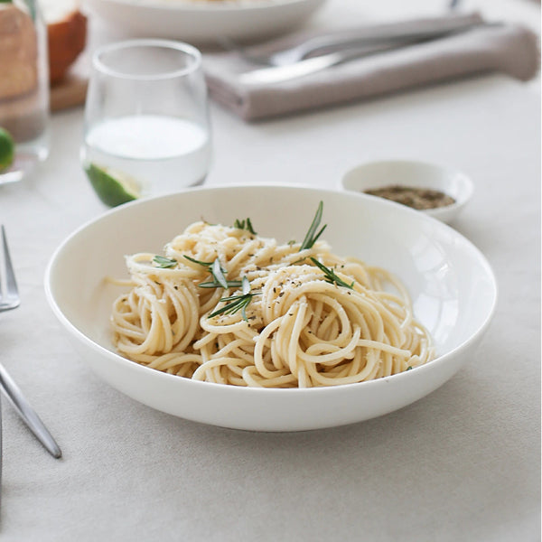 White bowl of spaghetti with herbs on a light gray surface