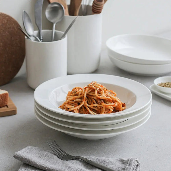 White ceramic bowls with spaghetti on a light gray surface, surrounded by kitchen utensils.
