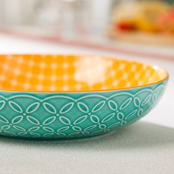 Ceramic bowl with orange top and teal bottom featuring a geometric pattern on a light surface.