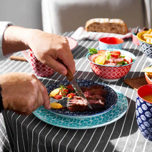Person cutting into a colorful ceramic plate of food with a table full of dishes in the background