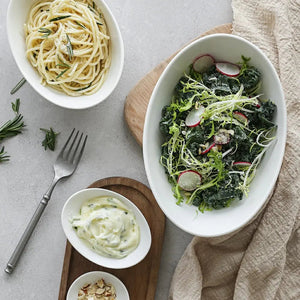 Two bowls of pasta and salad on a light surface with a fork and towel.