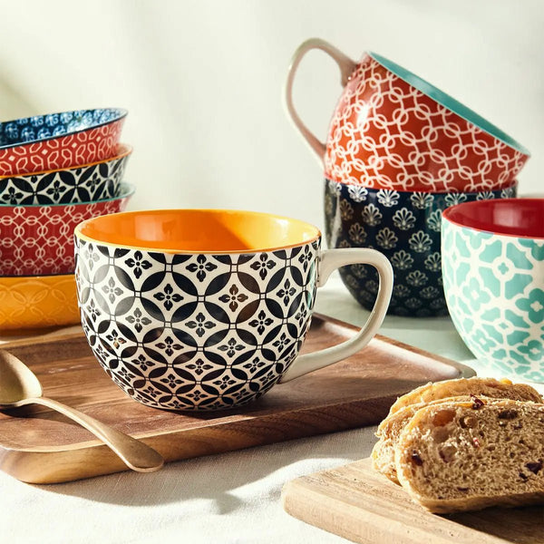Colorful patterned coffee mugs and bowls on a wooden tray with bread slices.