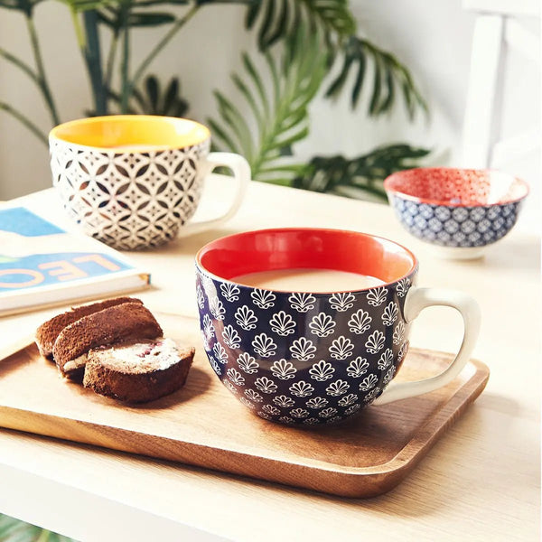 Patterned mugs on a wooden tray with pastries and a book,The mugs are filled with latte.