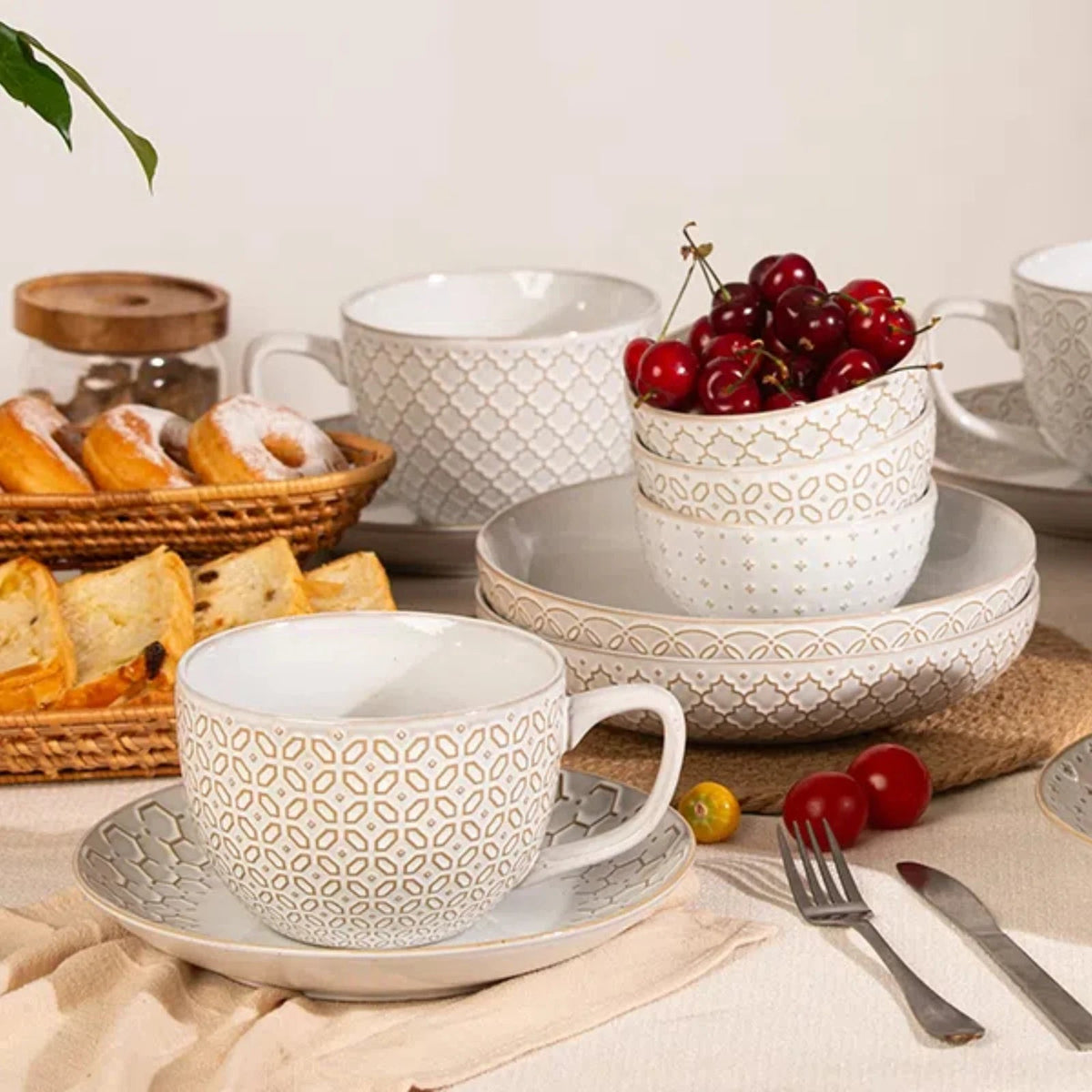 Ceramic tea set with patterned cups and saucers on a table with fruits and bread.
