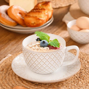Cup of coffee with berries and mint in large ceramic coffee mugs, with pastries and eggs in the background.